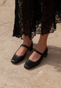 Scarpe Mary Jane nere in pelle testurizzata, con punta quadrata e tacco basso a blocco. Presentano un cinturino alla caviglia per una vestibilità sicura.