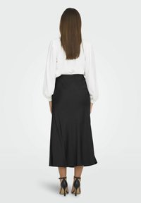 Jupe noire midi avec une texture lisse, dotée d'une taille ajustée et d'un léger évasement. Associée à une blouse blanche à manches longues et des talons noirs.