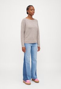 Maglione beige lavorato a maglia con scollatura rotonda, abbinato a jeans svasati azzurri chiari con pannelli laterali blu scuro e sneakers rosa.