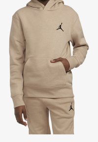 Felpa con cappuccio beige Jordan con tasca a marsupio e logo Jumpman nero sul petto. Abbinata a pantaloni della tuta beige, anch'essi con logo.
