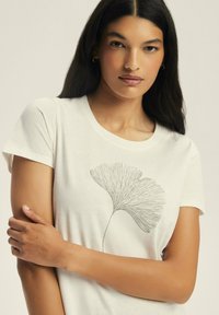 White T-shirt with short sleeves featuring a detailed green ginkgo leaf graphic on the front. Soft fabric with a relaxed fit.