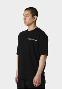 Svart bomullst-skjorte med rund hals og korte ermer, med hvit grafisk tekst på brystet. Slim fit med en glatt tekstur.