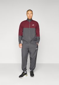 Completo sportivo Puma in grigio e bordeaux con giacca con zip e pantaloni elastici. Caratterizzato da dettagli con logo e maniche e caviglie elastiche.