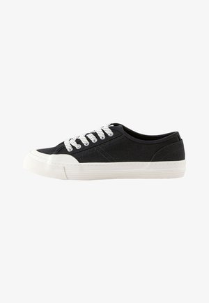 Niedriger schwarzer Canvas-Sneaker mit weißer Gummisohle, weißer Zehenkappe und weißen Schnürsenkeln.