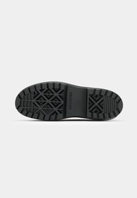 Soletta in gomma nera con superficie testurizzata, caratterizzata da un motivo a tasselli geometrici e con il marchio "Converse" sul lato.