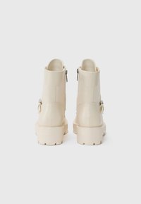 Bottines beiges à cheville avec une finition en cuir lisse, dotées d'une fermeture éclair et d'une semelle en caoutchouc épaisse pour une meilleure adhérence.