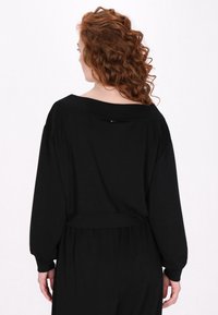 Top nero a maniche lunghe con scollatura ampia e vita arricciata. Tessuto morbido con una texture liscia, caratterizzato da dettagli di cucitura discreti.