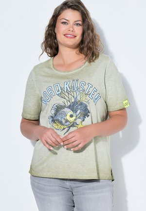 Uśmiechnięta kobieta o falowanych włosach nosi jasnozieloną koszulkę z ilustracją ryb, koralowców, rozgwiazdy oraz napisem "Nord Küsten".