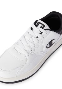 Białe sneakersy z czarnymi akcentami, wykonane z gładkiego materiału syntetycznego. Charakteryzują się teksturowanym wykończeniem, wiązanym designem oraz wyraźnym logo na języku.