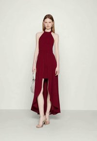 Μπορντό φόρεμα με λαιμόκοψη halter, ασύμμετρο κάτω μέρος, εφαρμοστό μπούστο και ροFlow φούστα. Συνδυασμένο με ασημένιες γόβες και μικρή τσάντα.