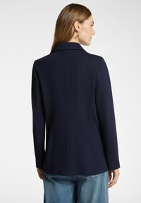 Marinblått figursytt kavaj med slagkrage, långa ärmar och en mjuk yta, kombinerat med ljusblåa högmidjade jeans.