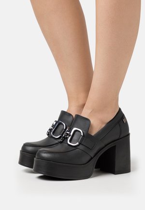 Chaussures à plateforme noires en cuir brillant, avec une large bride et un détail de boucle argentée, montées sur un talon haut et épais.