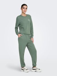 Sweat-shirt vert et jogging assorti en tissu doux, présentant une coupe décontractée, des poignets côtelés et des poches latérales. Accentué par un graphisme minimaliste.