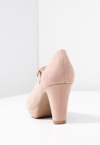 Scarpa con tacco alto in suede rosa, con punta arrotondata, una piccola fascia regolabile e una parte superiore texture. Il tacco è alto circa 10 cm.