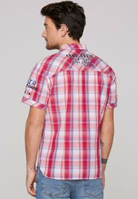 Kurzarmhemd mit kariertem Muster in Rot und Blau, mit geknöpftem Kragen. Enthält Logo-Details auf dem Rücken und den Ärmeln. Aus Baumwollmaterial.