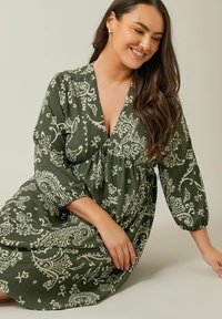 Vestido verde con estampado de paisley, escote en V, mangas de tres cuartos y cintura fruncida. Hecho de una tela texturada con un corte holgado.