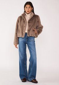 Veste en fausse fourrure marron avec col, munie d'une fermeture à boutons. Associée à un jean bleu à jambes larges et des chaussures marron. Texture lisse, design décontracté.