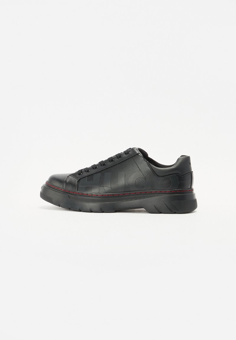 Basket en cuir noir avec une tige texturée, semelle épaisse, accents de couture rouge et lacets ronds. Présente un logo sur le côté.