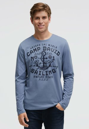 Long-sleeve, light blue t-shirt made of cotton featuring a printed graphic design with text about sailing and a nautical theme.