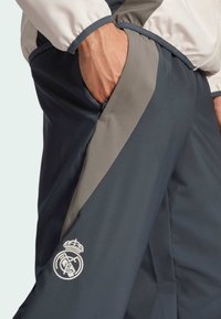Koninklijk blauwe trainingsbroek met grijze accenten, de stof is glad en lichtgewicht, met een ritszak en geborduurd logo op de linkerdij.