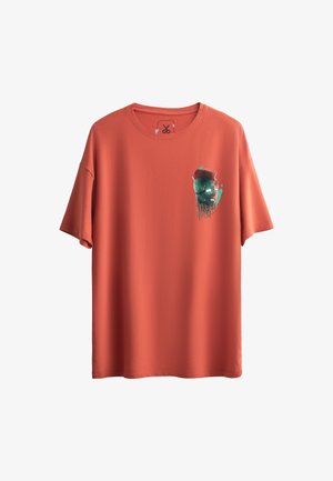 Korte mouw T-shirt in koraalkleur, gemaakt van zachte stof. Beschikt over een grafische afbeelding van een schedel met blauwe en groene accenten op de linker borst.