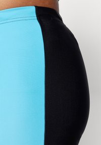 Színblokkolt szoknya, amely cyan kék és fekete panelből áll. Simább, rugalmas anyagból készült, látható varrással.