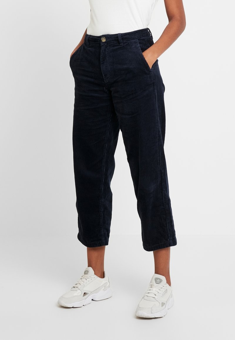 Marina blå kordbyxor med rak benner, som har sidofickor, knappstängning och en strukturerad yta. Åtsidos med vita sneakers.