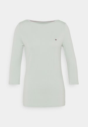 Chemise unie vert clair à manches longues avec un col rond et un petit logo Tommy Hilfiger sur le côté gauche de la poitrine.