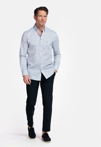 Chemise bleu clair à boutons avec un motif géométrique, associée à un pantalon sombre et des chaussures à enfiler noires. Comprend un col et des manches longues.