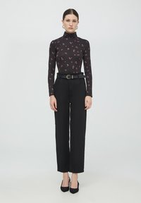 Maglietta nera a maniche lunghe con motivo floreale e collo alto, abbinata a pantaloni neri a gamba larga, fissati con una cintura nera e tacchi a punta.