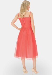 Koralowa sukienka z dopasowaną górą, cienkimi ramiączkami i detalem z sznurowaniem na plecach. Lekka, zwiewna, sięgająca do kolan, wykonana z lekkiego materiału.