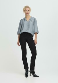 Hellblaue, drapierte Bluse mit V-Ausschnitt, kombiniert mit enganliegenden schwarzen Jeans und spitzen schwarzen High Heels. Schlichtes, sauberes Design.