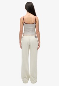 Grijs aansluitend tanktop met bordeauxrode bies, gecombineerd met losse, crèmekleurige joggingbroek, gezien van achteren. Soepele textuur, casual ontwerp.