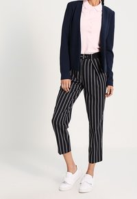 Blazer bleu marine, polo rose pâle et pantalon court rayé noir et blanc. Baskets blanches complètent la tenue. Look décontracté et moderne.