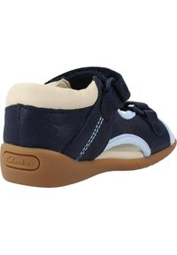 Zapato de cuero azul marino con acentos en azul claro y forro crema. Presenta una correa de Velcro y una suela de goma flexible. Diseño de punta redonda.