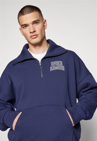Sudadera azul marino con cremallera de cuarto, con logo, de manga larga, corte oversize y bolsillos frontales. Tejido suave con puños y dobladillo acanalados.