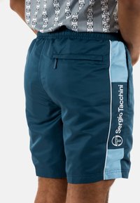 Pantalones cortos deportivos en color azul marino con panel lateral en azul claro, logo blanco, cinturilla elástica y bolsillo trasero. Fabricados con un tejido ligero y transpirable.