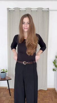 Czarna bluzka z długim rękawem zestawiona z czarnymi spodniami o wysokim stanie i szerokich nogawkach. Brązowy, teksturowany pasek z okrągłą klamrą spaja całość stroju.