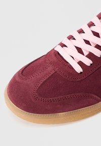 Bordo krēmveida zamšādas sporta apavs ar rozā šņorēm, raksturots ar gludu virsmu, apaļu purngalu un gumijas zoli ar reljefu rakstu.