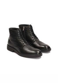 Botas de tobillo de cuero negro con un acabado liso, diseño de cordones, cremallera lateral y puntera redondeada. Suela de goma resistente para un mejor agarre.