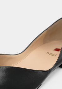 Black leather pump featuring a sleek design, pointed toe, and almond-shaped cut. Light beige insole with brand logo. Smooth texture.