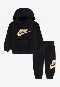 Fekete kapucnis pulóver és nadrág szett, puha anyagból készült, nagy arany Nike logóval az elülső részen és a bal nadrág szárán, bordázott mandzsettákkal.