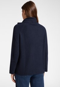 Dunkelblauer, gerippter Strickpullover mit hohem Kragen und langen Ärmeln, der ein einfaches Design und einen strukturierten Stoff aufweist. Rückansicht dargestellt.