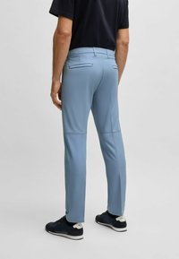 Light blue, slim-fit pants with a smooth texture, featuring rear pockets and seam detailing, paired with dark athletic shoes.