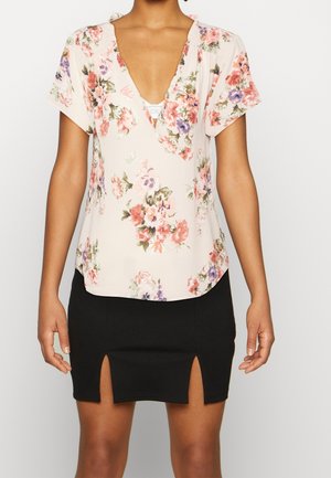 Top floreale a maniche corte di un delicato rosa pallido con scollatura a V profonda. Presenta fiori multicolori. Abbinato a una gonna aderente nera con spacchi laterali.