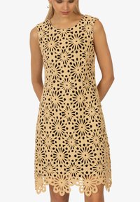 Spitzenkleid in hellem Beige mit floralem Cut-out-Muster. Ärmelloses Design mit rundem Ausschnitt und gewelltem Saum.