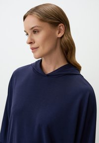 Felpa con cappuccio blu navy, dal taglio rilassato, con una texture morbida e un design minimale. Presenta un collo piccolo e una finitura del tessuto liscia.