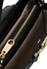 Zwarte leren handtas interieur met een gladde textuur, voorzien van een gouden rits en een beige voering. Inclusief kleine hardware details.