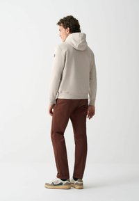 Světle šedá mikina s kapucí, hnědé kalhoty a bílé tenisky s šedými a zelenými akcenty, minimalistický design a měkká textura.