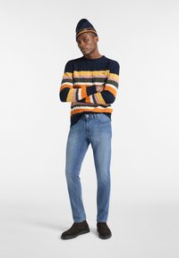 Maglione a maglia multicolore con ampie righe in blu scuro, arancione, giallo e rosa, abbinato a jeans slim fit blu chiaro e stivali marrone scuro.